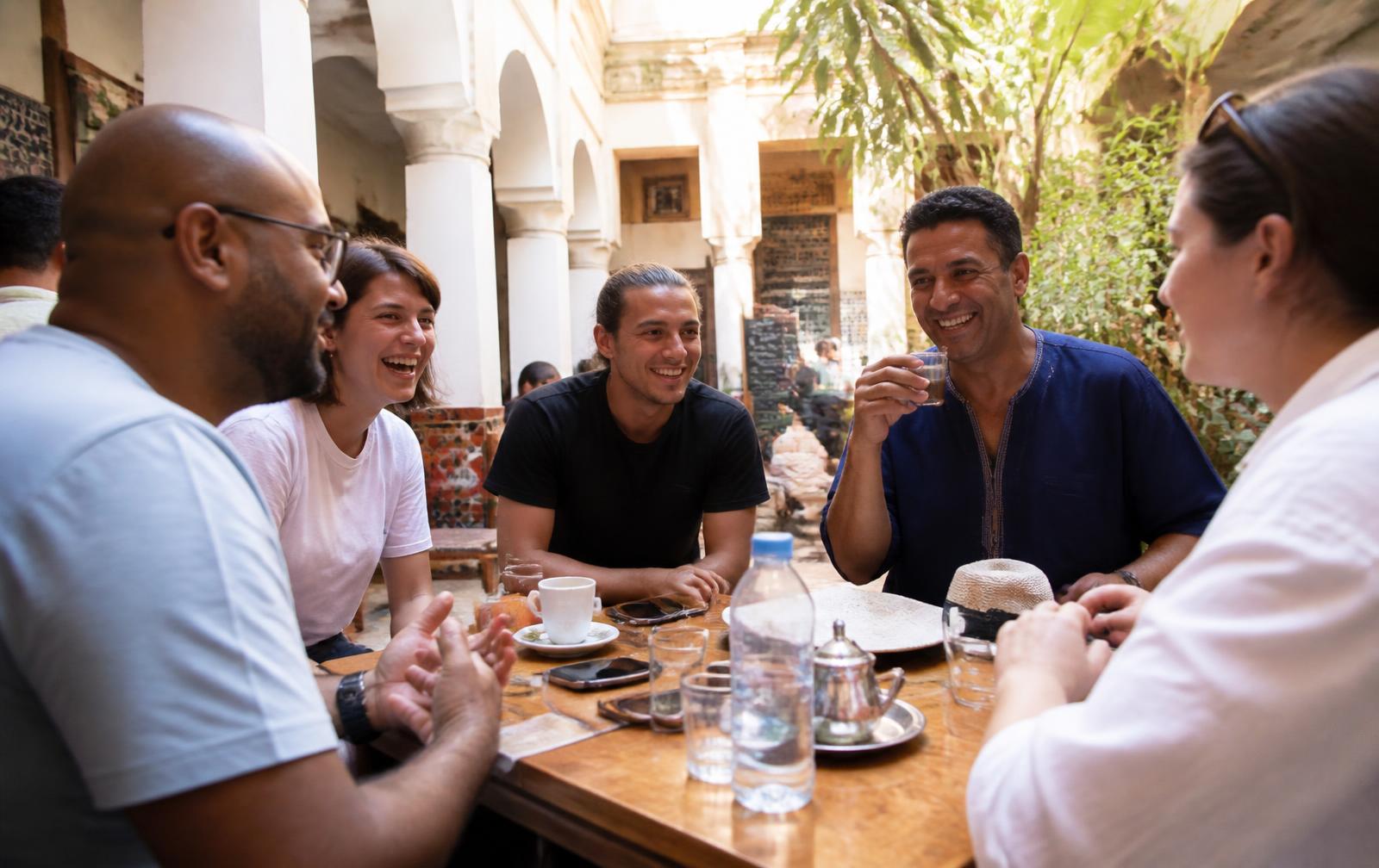 Travellers and locals talking around a table in a sunlit courtyard cafe