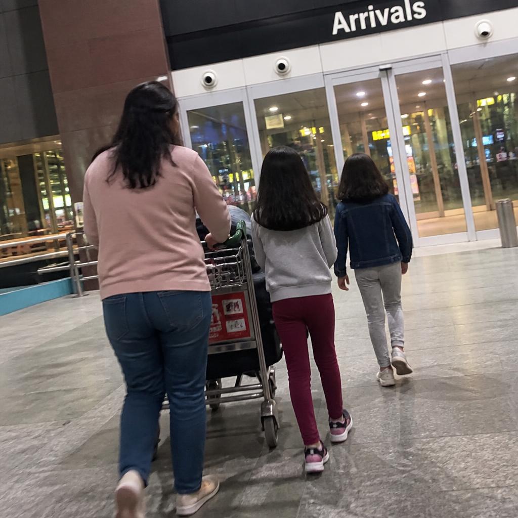 A family walking with luggage through an airport arrivals hall at night